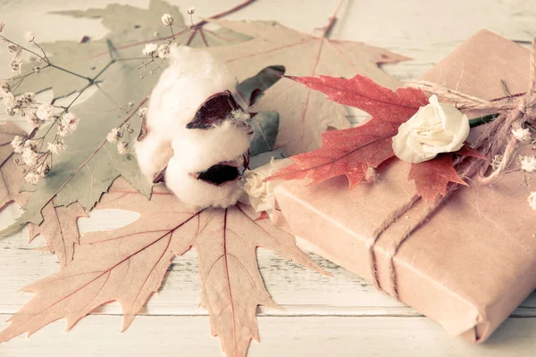 fallen  maple leaves,  gift box, sprig of white flowers and cotton on a white wooden