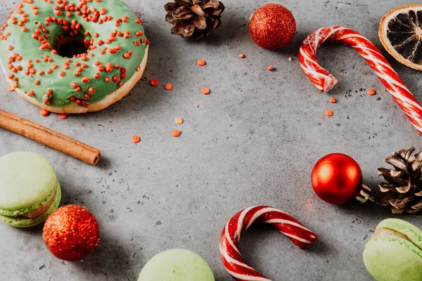lollipops, cone, cinnamon stick, green doughnut, cookies, macaroon, red Christmas balls on a gray background, Christmas sweets