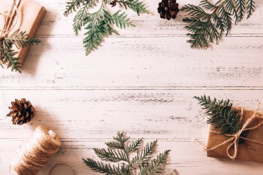 İçinde köknar dalları olan hediye kutuları, beyaz ahşap bir arka planda ip, koni ve yeşil thuja dalları olan bir makara.