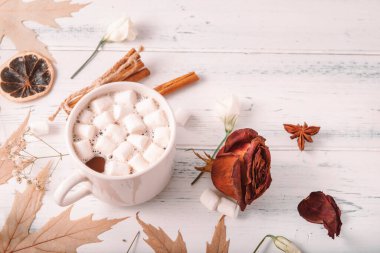 Sıcak çikolata, marşmelovlu kakao, sonbahar sarısı akçaağaç yaprakları, koniler, tarçın çubukları, beyaz ahşap arka planda kurumuş gül.