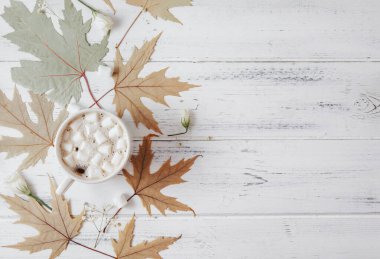 Bir fincan kremalı sıcak çikolata, beyaz ahşap arka planda akçaağaç yaprakları, kopyalama alanı.