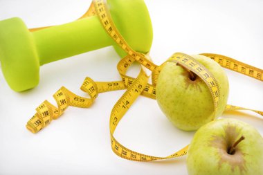 1 dambıl, 2 yeşil elma, beyaz arka plan görünümlü sarı mezura.