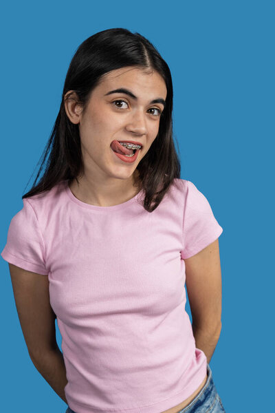 Игривая молодая женщина с зубными скобками торчит языком на ярком синем фоне