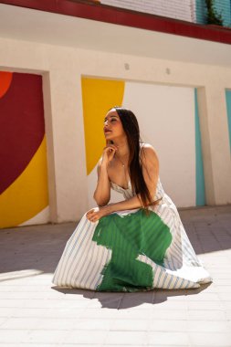 Modern bir şehir ortamında canlı, geometrik olarak boyanmış bir duvara karşı düşünceli bir şekilde duran şık bir model.