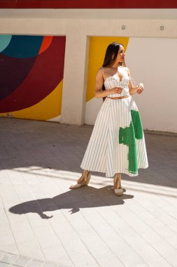 Moda mankeni, renkli, canlı bir duvara karşı poz veren, üzerinde yeşil lekeler olan şık çizgili iki parçalı bir kıyafet sergiliyor.