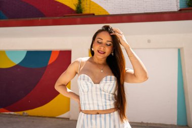 Hareketli ve renkli bir duvar resminin önünde eli saçında, gözleri kapalı poz veren modacı.