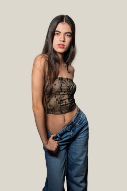 Modayı takip eden genç bir kadın stüdyo ortamında kendine güvenerek poz veriyor, modaya uygun bir kıyafet giyiyor ve benzersiz tarzını sergiliyor.