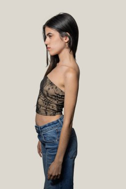 Profilde poz veren genç bir kadının atölye fotoğrafı. Kot pantolon ve bluz giyiyor.