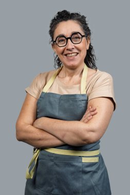 Kameraya gülümseyen kendine güvenen girişimci kadın kollarını kavuşturmuş bir önlük giyiyor.