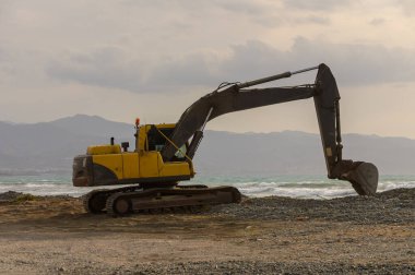Kıbrıs 'ta kumlu bir sahilde sarı kazıcı, mavi Akdeniz suları yakınında çalışıyor..