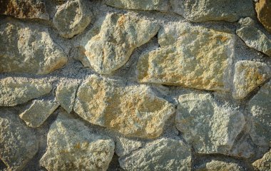 Güneş ışığının yüzeyi boyunca aktığı doğal bir taş duvara yakın çekim. Tasarım, mimari veya açık hava projeleri için sıcak güneş ışınlarına sahip kırsal doku.