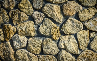 Güneş ışınlarının gölgeler ve röfleler yarattığı dokulu taş bir duvarın makro görüntüsü. Mimarlık, açık hava veya tasarım projeleri için ideal.