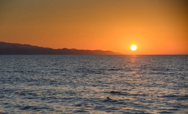 Kıbrıs 'ta güneş Akdeniz' e batarken gün batımı manzarası. Sakin su ve romantik akşam atmosferiyle altın saat deniz manzarası.