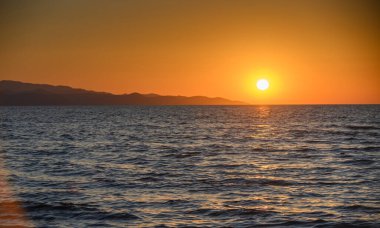 Kıbrıs, Morphou Körfezi 'nde güzel bir gün batımı. Huzurlu Akdeniz 'e yansıyan altın ışık huzurlu ufuk ve sakin kıyı manzarası.