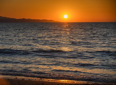 Kıbrıs 'taki Morphou Körfezi' nin üzerinde altın gökyüzü ve sakin Akdeniz manzaralı bir gün batımı. Sahil şeridinin ve doğanın huzurlu akşam manzarası.