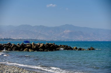 Kıbrıs körfezinin kayalık kıyı şeridinde bir balıkçı balık yakalıyor. Açık deniz manzarası, doğal ışık, otantik balıkçılık etkinliği seyahat ve yaşam tarzı fotoğrafçılığı için mükemmel..