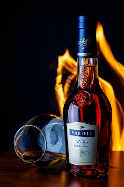 Gaziveren, Kıbrıs Rum Kesimi 06.01.2025 Martell konyak şişesi iki konyakla birlikte ahşap bir masada yatıyor. Arka planda sıcak alevler lüks ve rahat bir atmosfer yaratır..