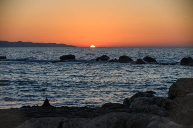 Kıbrıs 'ta dağları ve Akdeniz' i olan güzel bir yaz günbatımı. Sakin suyun üzerindeki ılık altın ışık sakin ve romantik tatil manzarası yaratır. Kıbrıs Dağları ve Akdeniz 'de daha güneşli bir gün batımı