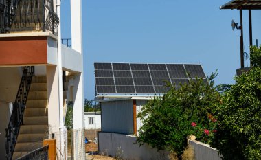 Küçük bir Kıbrıs köyünün çatılarına kurulmuş güneş panelleri, Akdeniz güneşi altındaki temiz yenilenebilir enerji, sürdürülebilir yaşam ve ekolojik teknolojiyi sembolize ediyor.