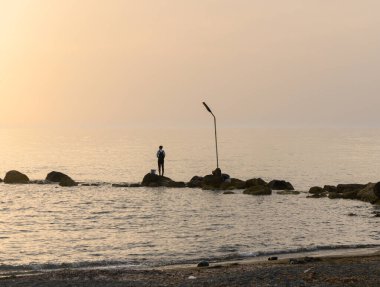 Yalnız bir balıkçı, Kıbrıs Rum Kesimi 'nin çarpıcı bir gün batımında kıyı kayalarından denize kendi hattını atıyor.