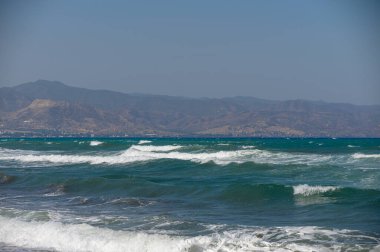 Akdeniz 'in güzel dalgaları ve Kıbrıs' ın ufuklarında uzak dağlar. Yaz atmosferli doğal kıyı manzarası.