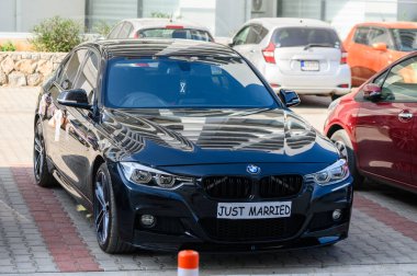 Gaziveren, Kıbrıs 06.14.2025 Şık siyah BMW Bir sokakta Yeni Evli tabelasıyla, şenlikli düğün atmosferlerini ve lüks araçları yakalıyor.