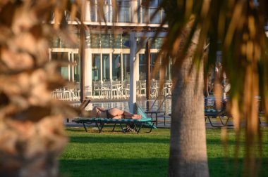 Siyah mayo giymiş genç bir kadın, güneşli bir sandalyede güneşleniyor, açık havada yaz tatilinin tadını çıkarıyor.