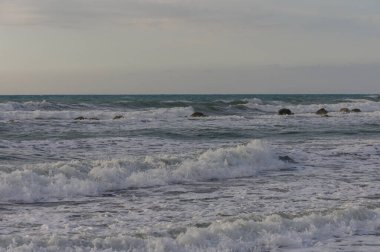 Kıbrıs 'taki bir Akdeniz sahilinde kayalara çarpan güçlü deniz dalgaları. Okyanus enerjisi ve doğal dokuları ile dinamik kıyı sahnesi.