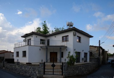 Kıbrıs 'ın güneşli bir köyünde sakin bir caddede Akdeniz tarzında büyüleyici beyaz duvarlı bir ev..