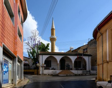 Kıbrıs 'ın Lefke kentindeki tarihi cami, yerel binalar ve dağlarla çevrili uzun bir minare ve geleneksel İslami mimariye sahip.