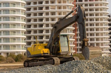 Kıbrıs 'ta Akdeniz kıyısında çalışan ağır sarı bir kazıcı. Bir kıyı manzarasında sanayi faaliyeti.