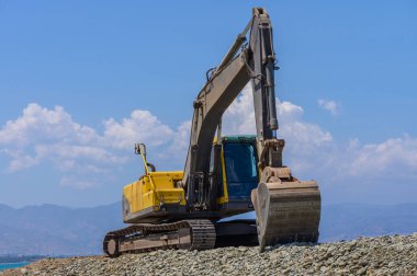 Kıbrıs 'taki bir Akdeniz plajında faaliyet gösteren sarı kazıcı, kıyı bakımı sırasında kum seviyesini yükseltiyor. Açık gökyüzü, arka planda deniz.