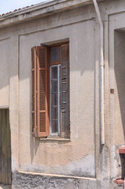 Sıcak öğleden sonra ışığı, bu sakin köyde geçmişteki hikayeleri ima ederek, yıpranmış ahşap panjurlarla bezenmiş kırsal bir duvara dökülüyor. Zaman, güzelliğin ortasında duruyor..