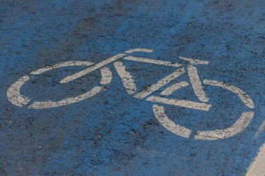 Canlı bir bisiklet sembolü, kentsel alanda canlı bir mavi kaldırıma karşı duruyor, bir bisiklet yolunu vurguluyor ve şehirde çevre dostu ulaşım seçeneklerini teşvik ediyor.