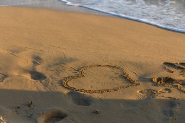 Kumlu bir kalp kıyı şeridinde usulca kıvrılır dalgalar alacakaranlıkta sahili nazikçe öperken.