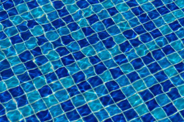 Parlak güneş ışığı altında, titreyen dalgalar, sakin bir yüzme havuzunun mavi fayanslı yüzeyinde dans eder..