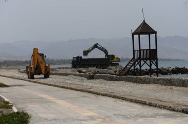 Yüksek çözünürlüklü sarı kazıcı, kıyı şeridi inşaatı sırasında Kıbrıs 'ın Akdeniz kıyısındaki bir çöp kamyonuna büyük deniz taşları yüklüyor..