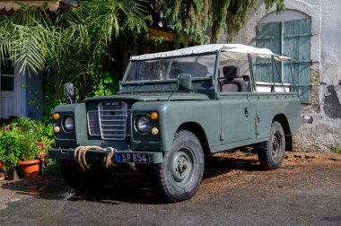 Kıbrıs 'ta sakin bir sokağa park etmiş eski yeşil Land Rover klasik tasarım ve Akdeniz kentsel atmosferini sergiliyor.