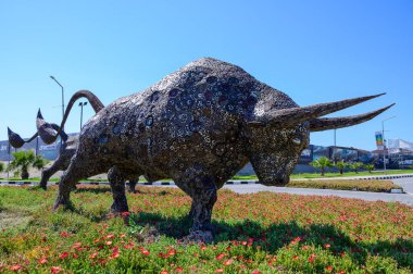 Çimenlerdeki çelik boğa heykelleri, önde gelen bir cami ve arka planda uzun minareler. Kuzey Kıbrıs kültür sahnesi.