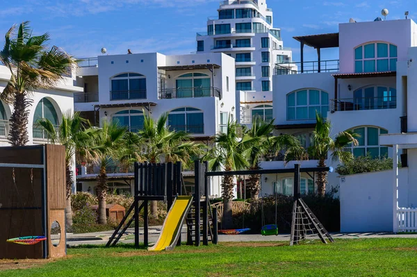 Ekipmanlarla dolu canlı bir oyun alanı berrak mavi gökyüzünün altında, sahil kenarındaki zarif evlerin yanında duruyor..