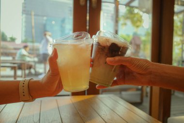 İki kişi bardakları tokuşturur, buzlu kahve ve limon suyu ile kadeh kaldırır..