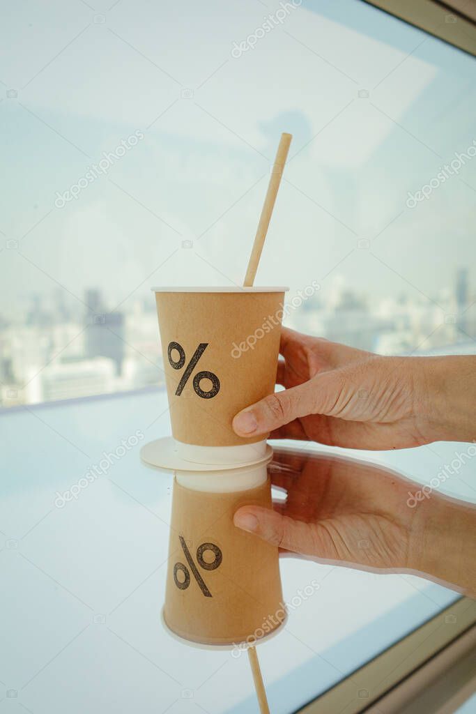 A person's hands hold brown coffee cup with a percent logo and a straw.