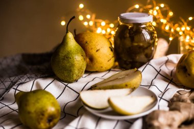 Fotoğraf taze armut, reçel ve masa örtüsü arka planda zencefil kökü bir kavanoz gösterir.
