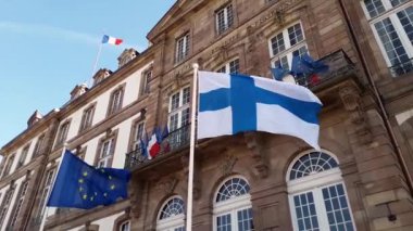 Fransa 'nın başkenti Htel de Ville de Strasbourg' un önünde Finlandiya ve Eu bayraklarını mavi gökyüzü arka planına karşı dalgalandıran rüzgar.