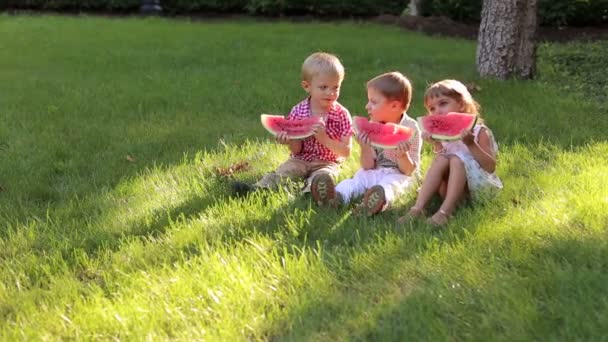 Tři veselá šťastné děti jíst meloun v létě v parku.