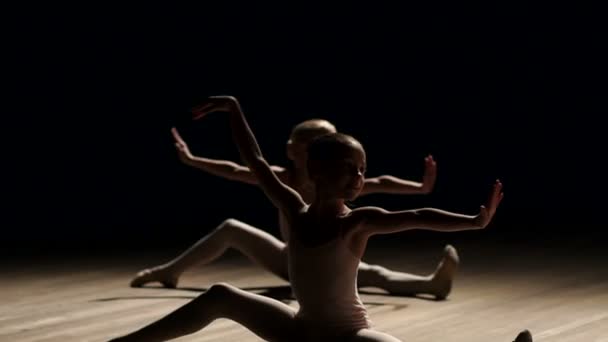 zwei kleine Mädchen tanzen Ballett auf der Bühne im Dunkeln auf einem Holzboden.