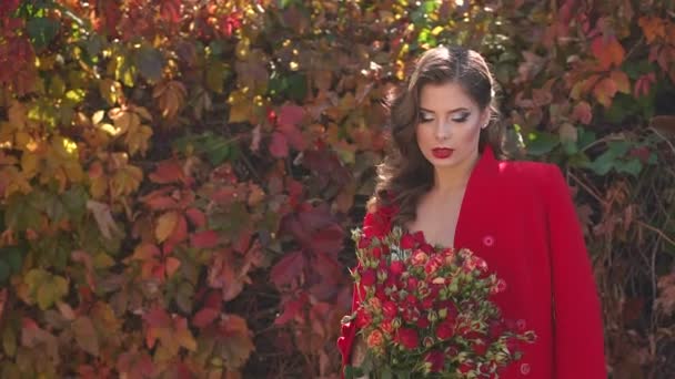 Girl in a dress and a red coat with a bouquet of flowers in an autumn Park. — Stock Footage Girl in a dress and a red coat with a bouquet of flowers in an autumn Park. Royalty Free Stock Footage