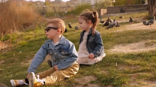 Two small three-year-old children sit on the Bank of the river in the Park. — Stock Footage Two small three-year-old children sit on the Bank of the river in the Park. Royalty Free Stock Video