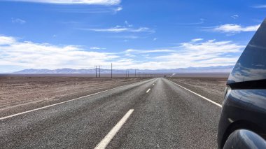 Şili 'nin Tarapac bölgesinde, Atacama' da çöl manzarası boyunca düz asfalt yolda giderken daha büyük bir arabanın önünde. Seyahat, yolculuk, turizm, tatil, ulaşım