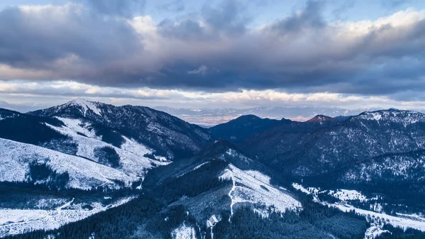 Drone, kısmen karla, kısmen de Jasna, Low Tatras, Slovakya 'daki ağaçlarla kaplı dağ öfkesini yükseltti. Avrupa 'daki Karpatya Dağları' ndaki kayak merkezinin kasvetli gökyüzünün karlı fotoğrafı.. 